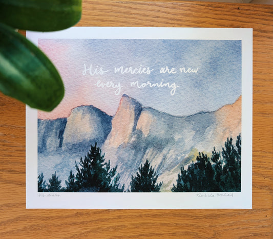 Art print with mountain landscape and 'His mercies are new every morning' text on a wooden surface.