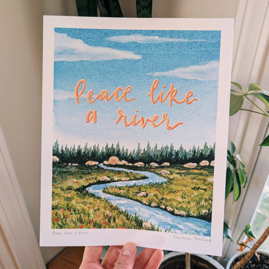 Art print with a scenic landscape and 'Peace like a river' text, held by a person.
