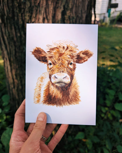 Hand holding a card with a cow illustration outdoors.