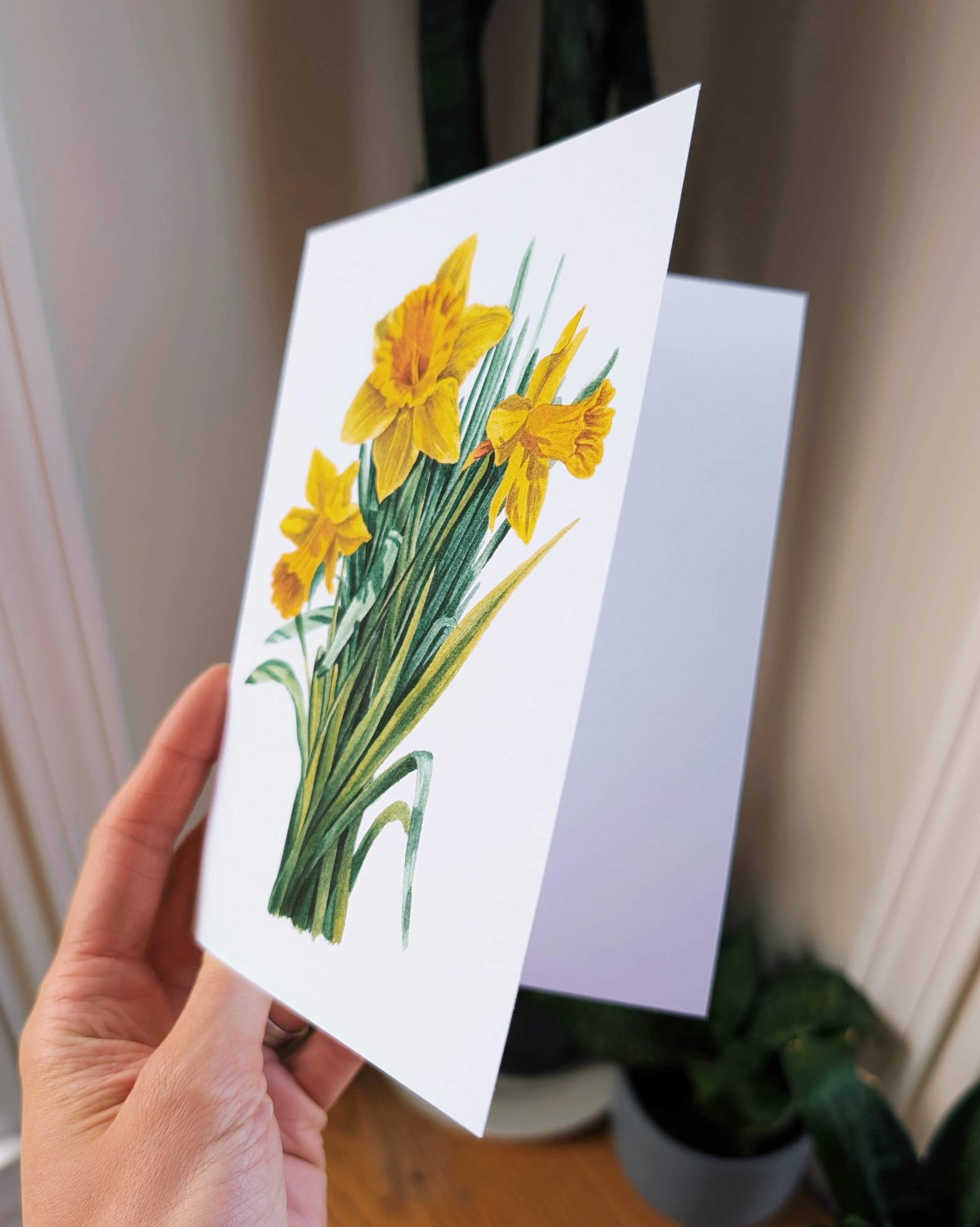 Hand holding a card with a daffodil illustration.