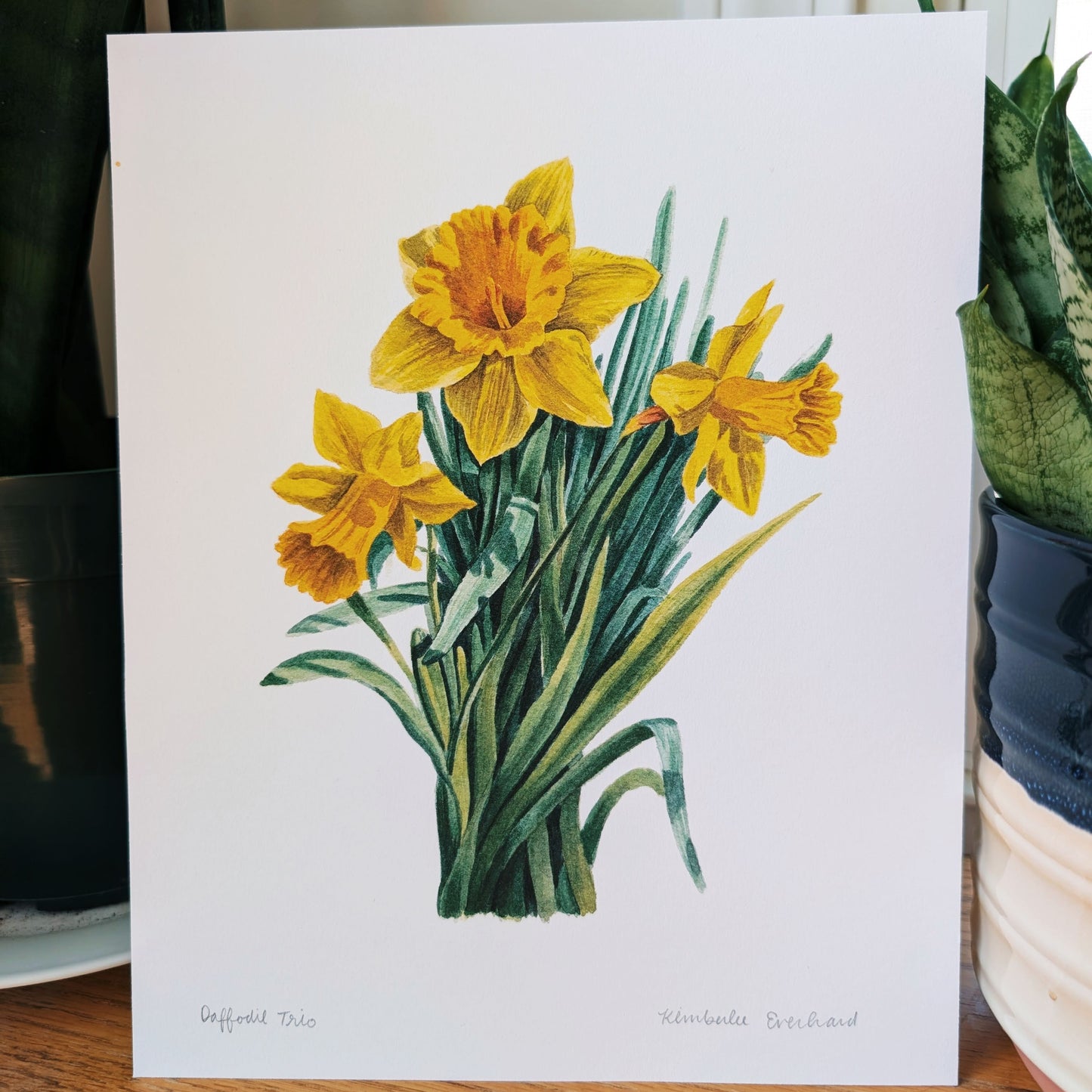 Greeting card with yellow daffodil illustration on a wooden surface.