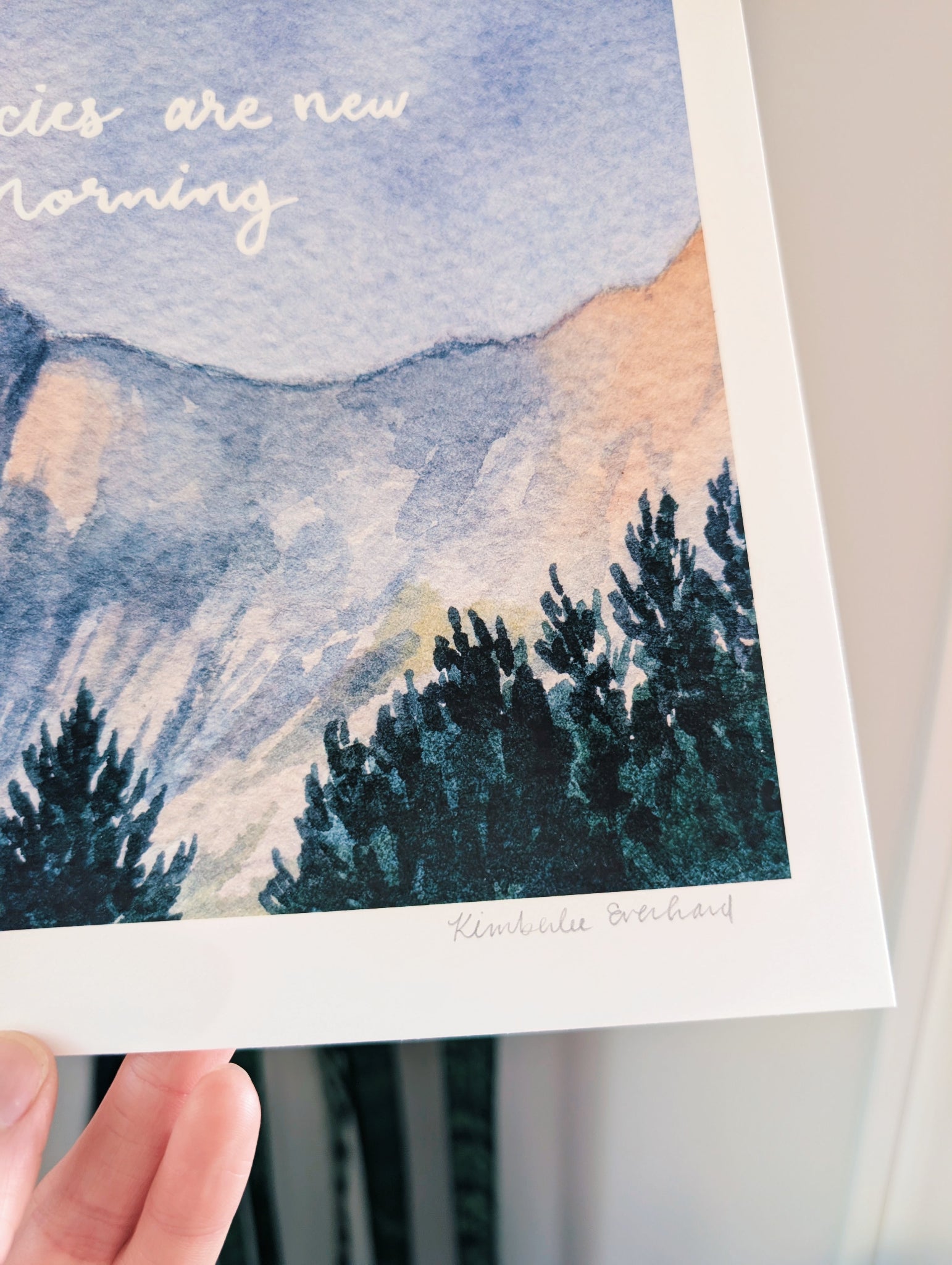 Art print with mountain and tree landscape and text 'Species are new morning' held by a hand.