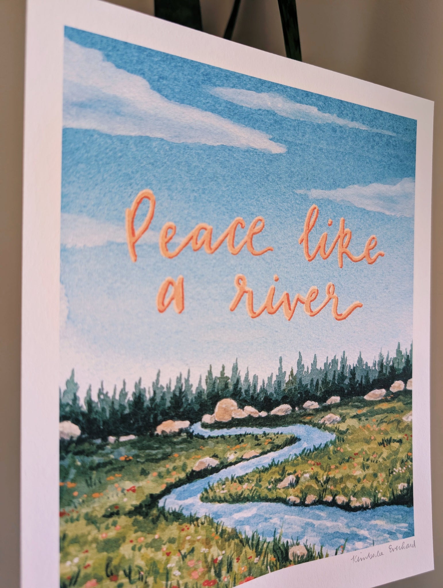 Art print with a river scene and 'Peace like a river' text on a blue sky background.