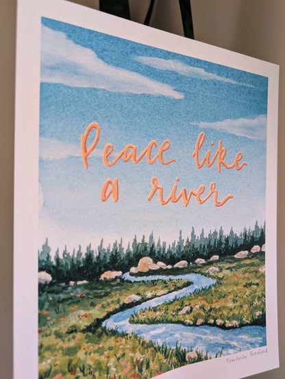Art print with a river scene and 'Peace like a river' text on a blue sky background.