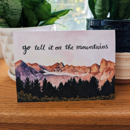 A card featuring a painted mountain landscape with the phrase 'go tell it on the mountains' in script at the top.